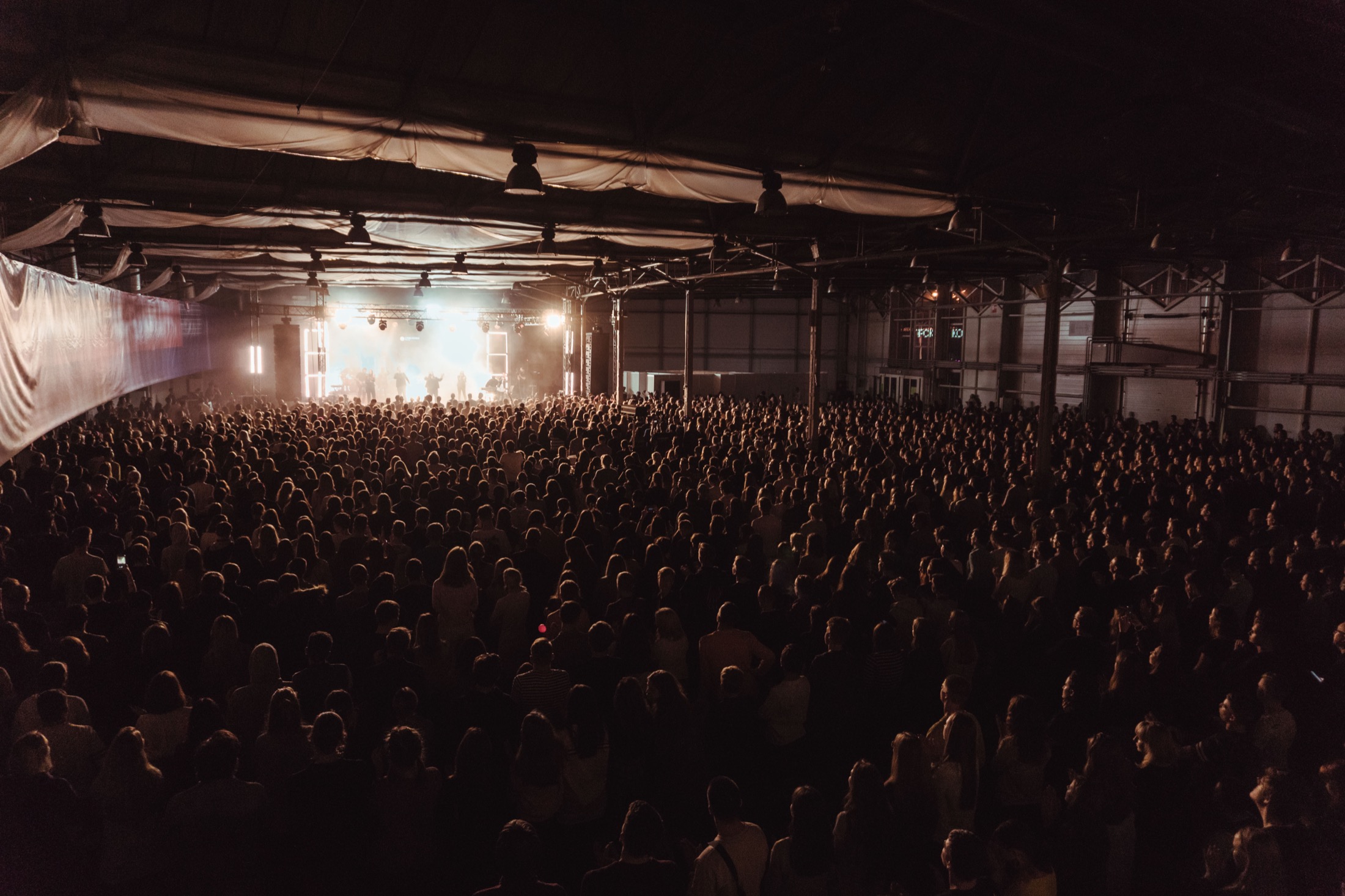 Grande salle de concert plongée dans la lumière, avec une scène et un public dense.